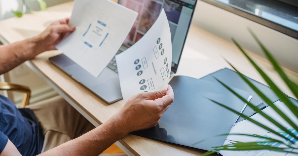 Designer care verifică schițele unui site lângă laptop
