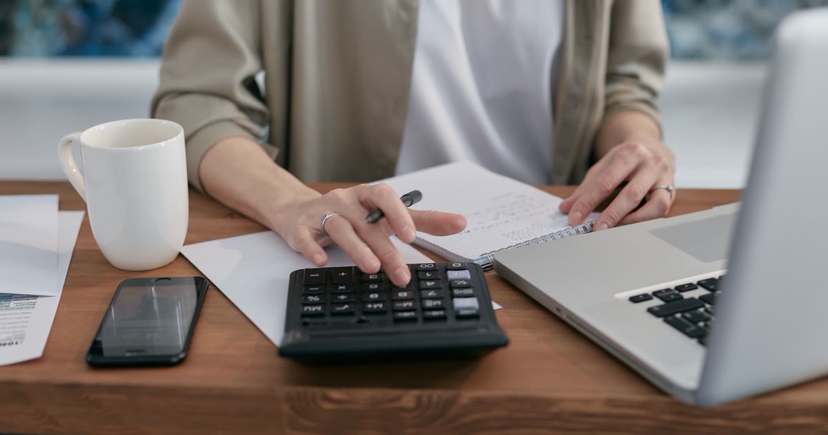 Persoană care calculează bugetul de promovare lângă un laptop